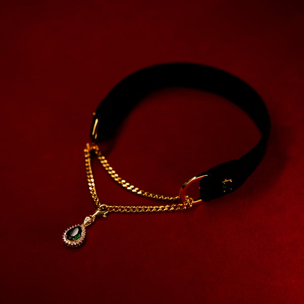 Black velvet choker with gold chain and green gemstones on a red background