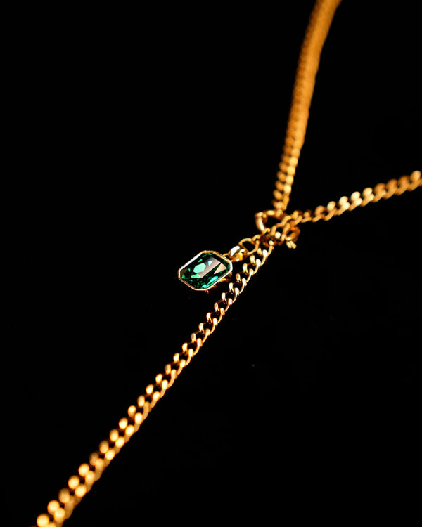 Gold chain necklace with a green gemstone pendant on a black background